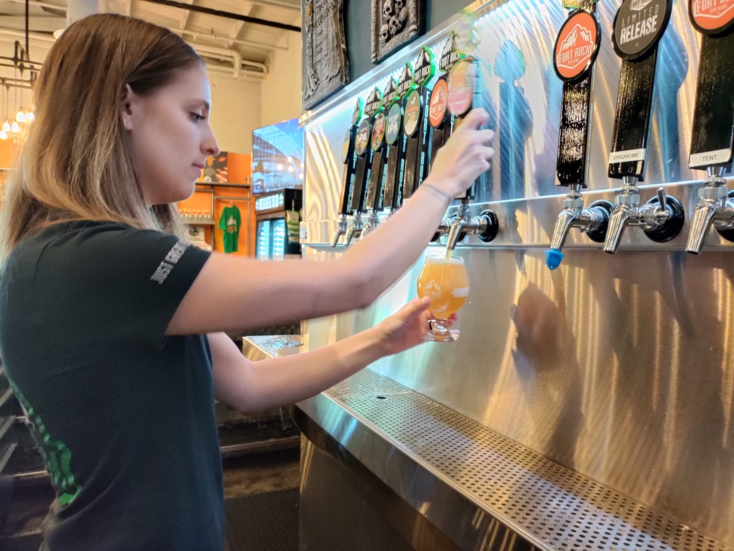 Woman pours a beer from a row of tap handles in a brewery.